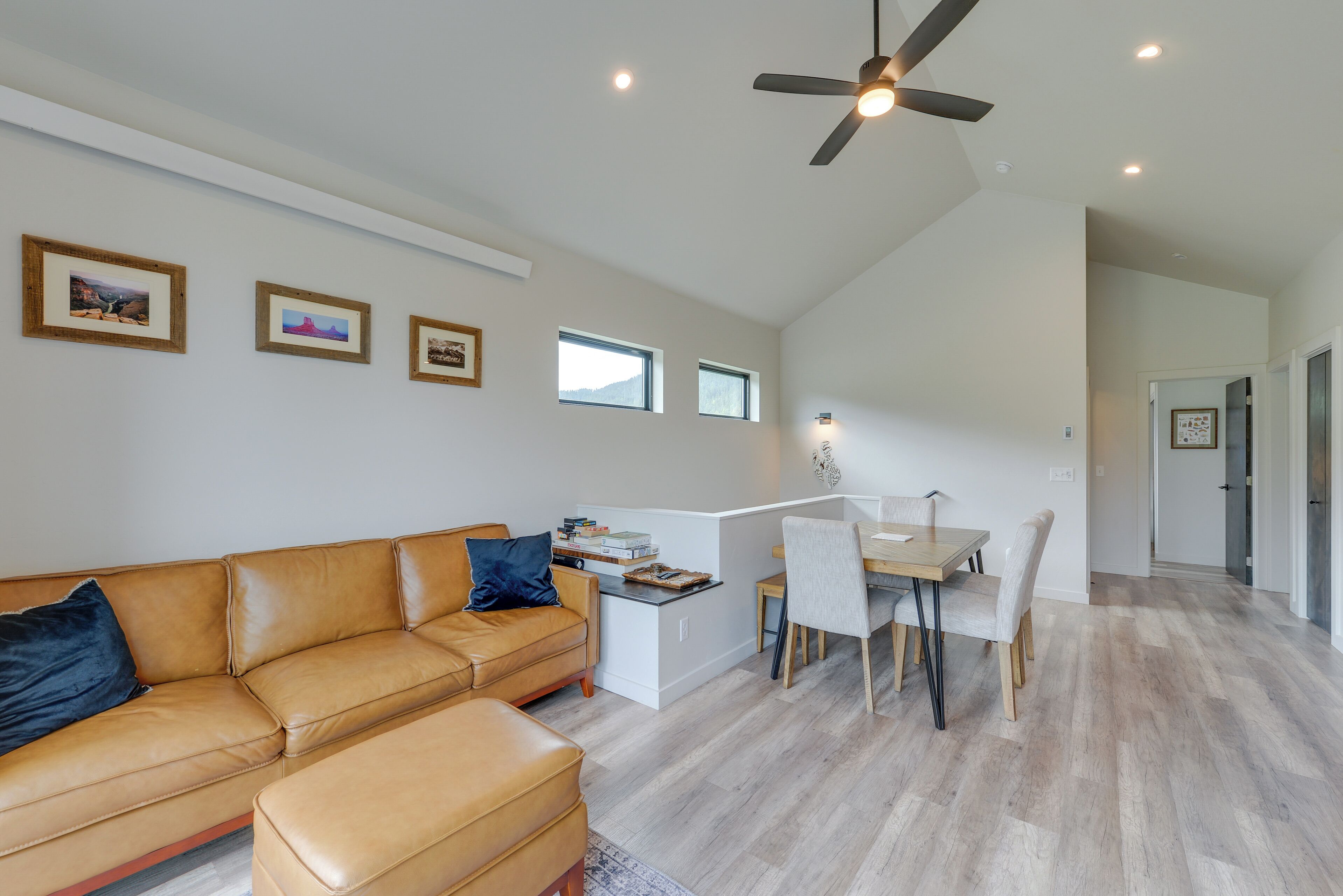 A spacious living area with a tan leather sofa, a dining table with chairs, and a ceiling fan.