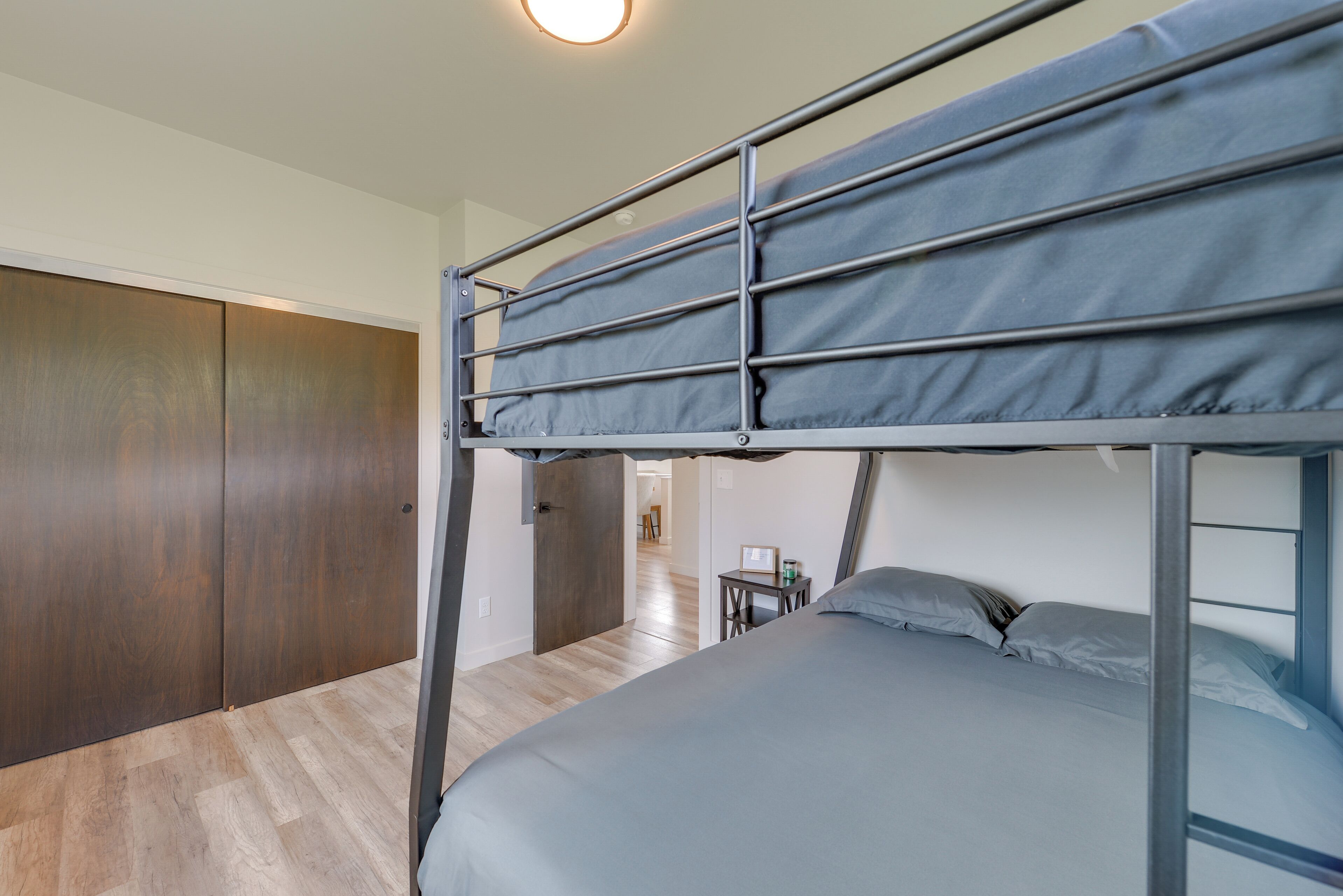 A bunk bed with a desk and chair, a wardrobe, and a hallway leading to another room.