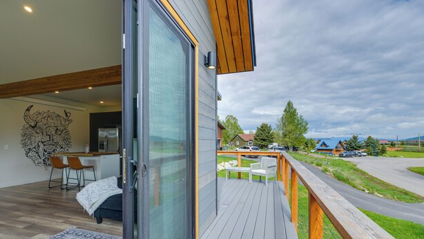 Une maison moderne dotée d’une grande porte-fenêtre coulissante qui donne sur un balcon avec une terrasse en bois et un espace salon extérieur.