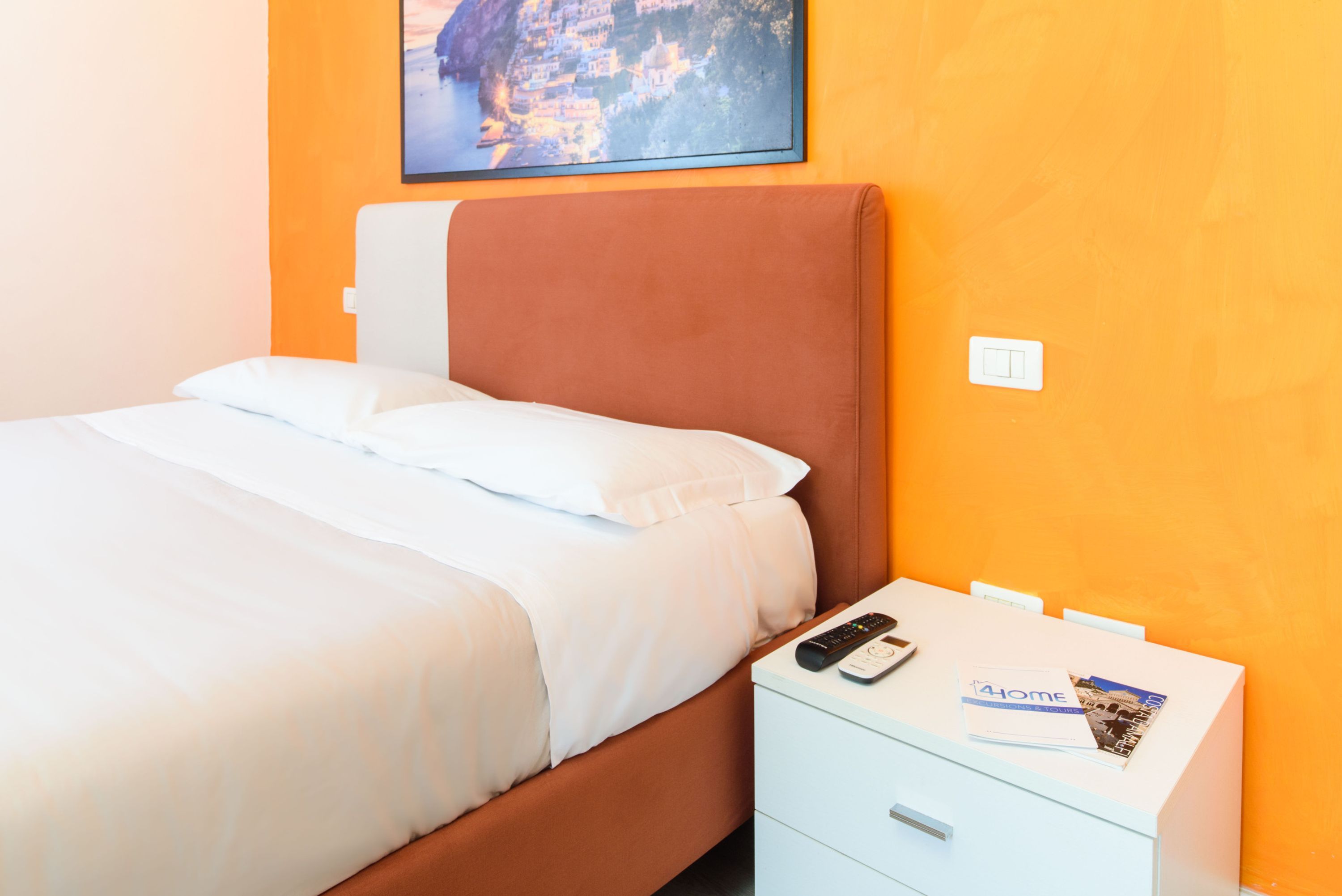 A hotel room with a bed, a nightstand, a remote control, and a brochure.