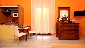 Una cocina compacta con microondas, pileta y alacenas, un comedor con mesa y sillas, y un aparador de madera con espejo.