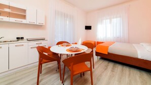 Una habitación de hotel moderna con cama, una mesa de comedor con sillas, una zona de cocina con armarios y un televisor montado en la pared.