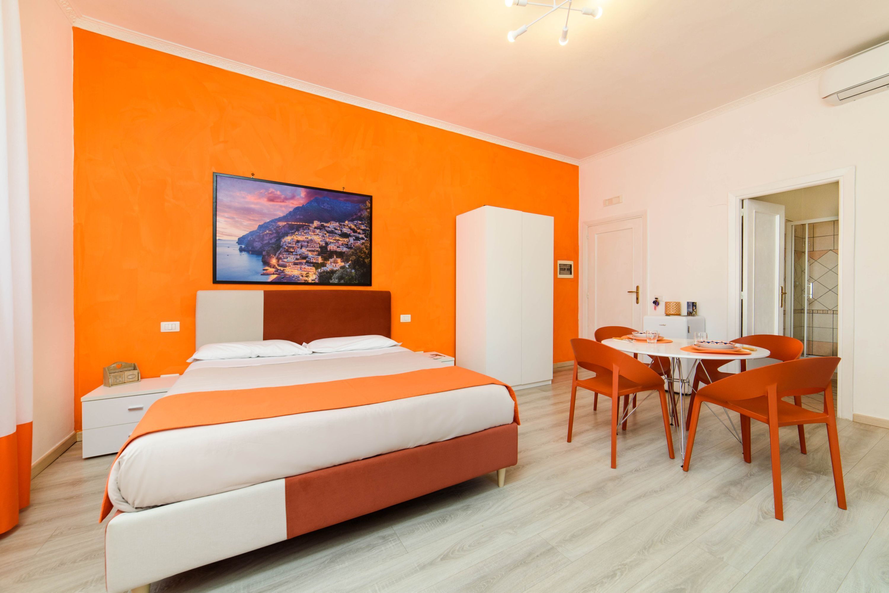 A hotel room with a large bed, a dining table with chairs, and a painting on the wall.