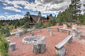 A lodge with a stone fire pit and wooden benches, surrounded by a forested area. - Big Family Fun! Mtn Cabin Between Bryce & Zion (Duck Creek Village)