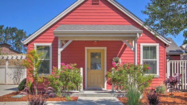 A red single-story house with a front porch, a small garden with pink flowers, and a clear blue sky. - Serene Bungalow-style Home in Point Reyes Station! (Point Reyes Station)