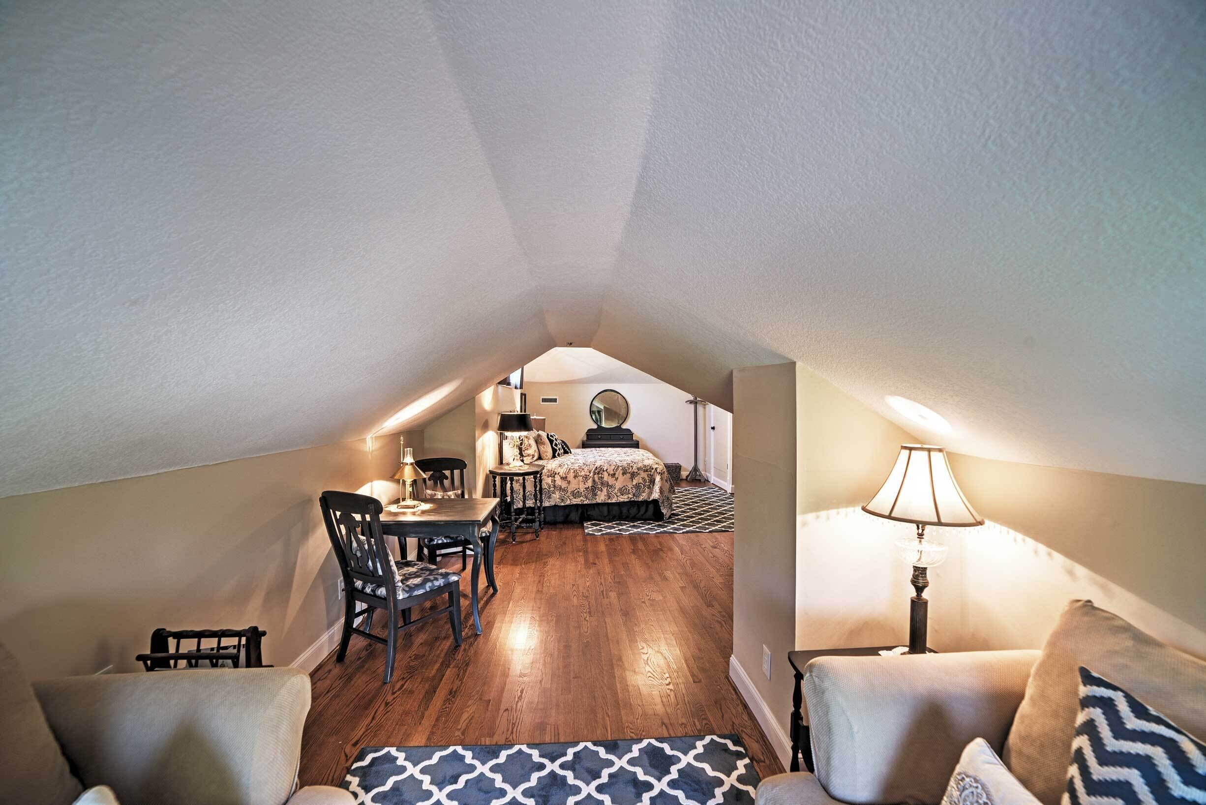 An attic bedroom with a dining area, a bed with patterned bedding, and a lamp.