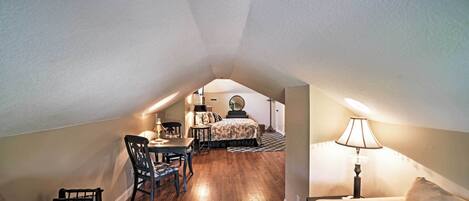 An attic bedroom with a dining area, a bed with patterned bedding, and a lamp.