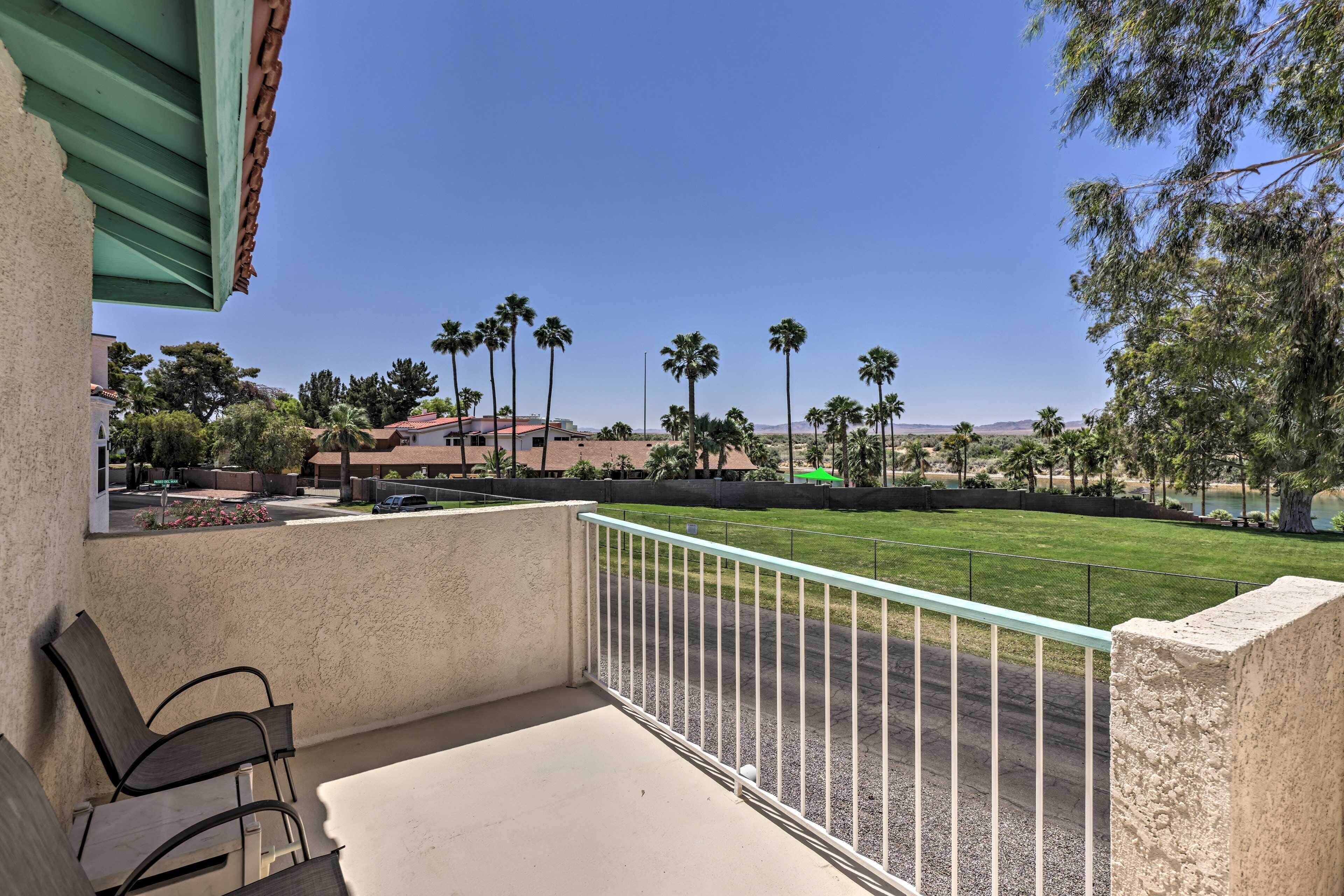 A balcony with a view of a green lawn, palm trees, and distant hills.