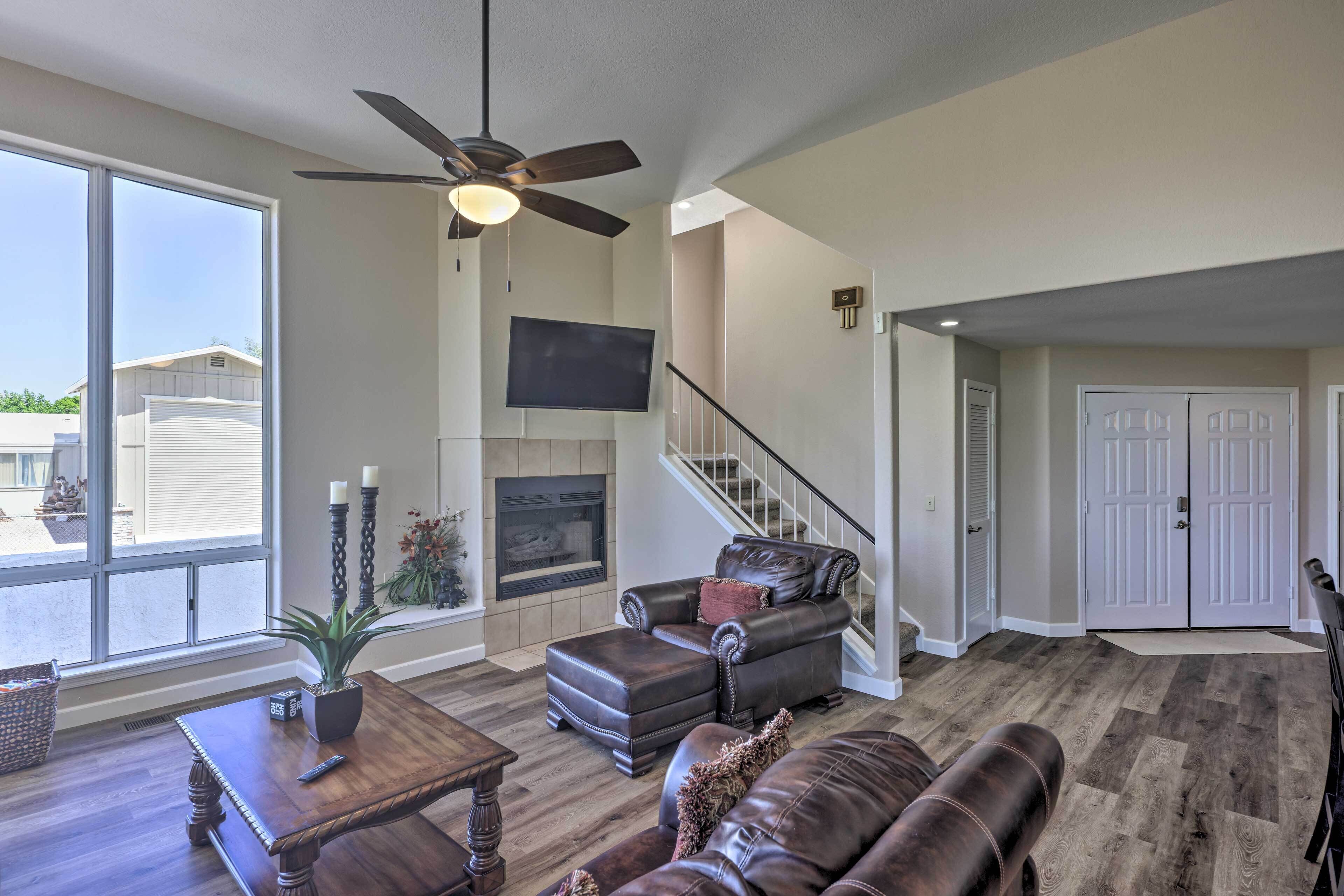 A spacious living room with a fireplace, leather furniture, a ceiling fan, and a large window.