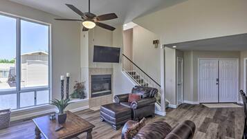 A spacious living room with a fireplace, leather furniture, a ceiling fan, and a large window.