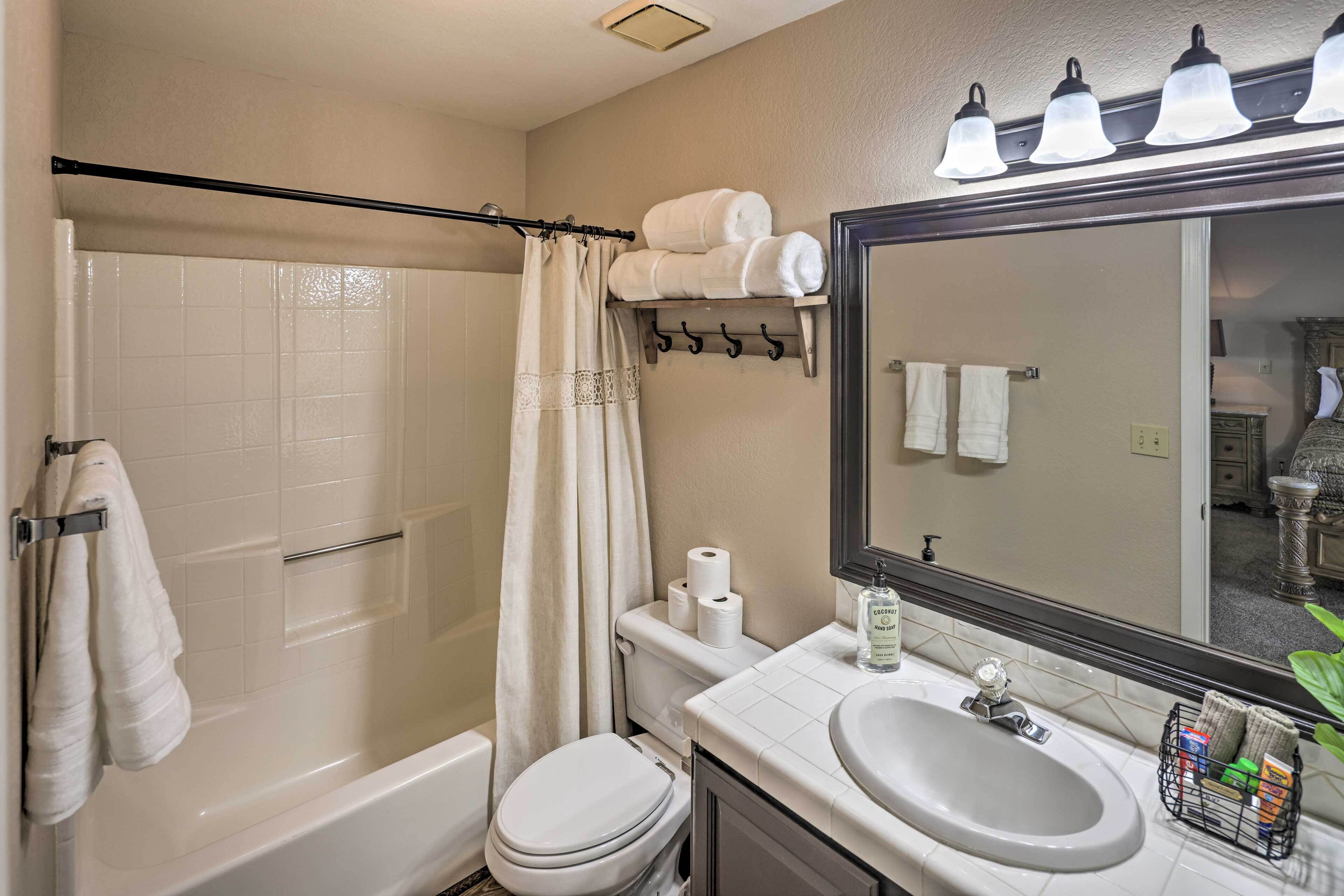 A bathroom with a bathtub, toilet, sink, and a mirror with lights above.