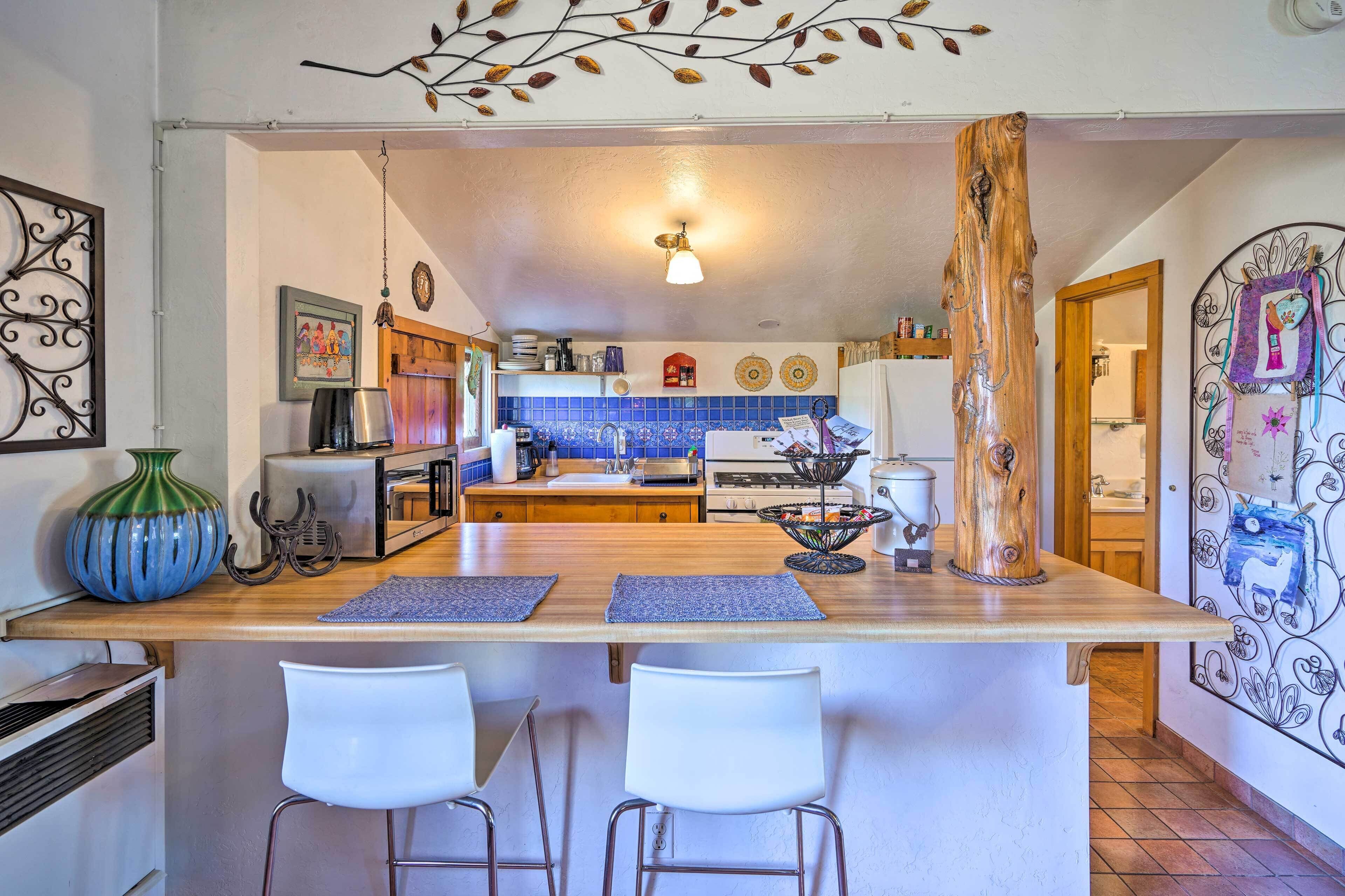 Una cocina con una isla de madera, taburetes blancos tipo barra y un tronco de árbol decorativo.