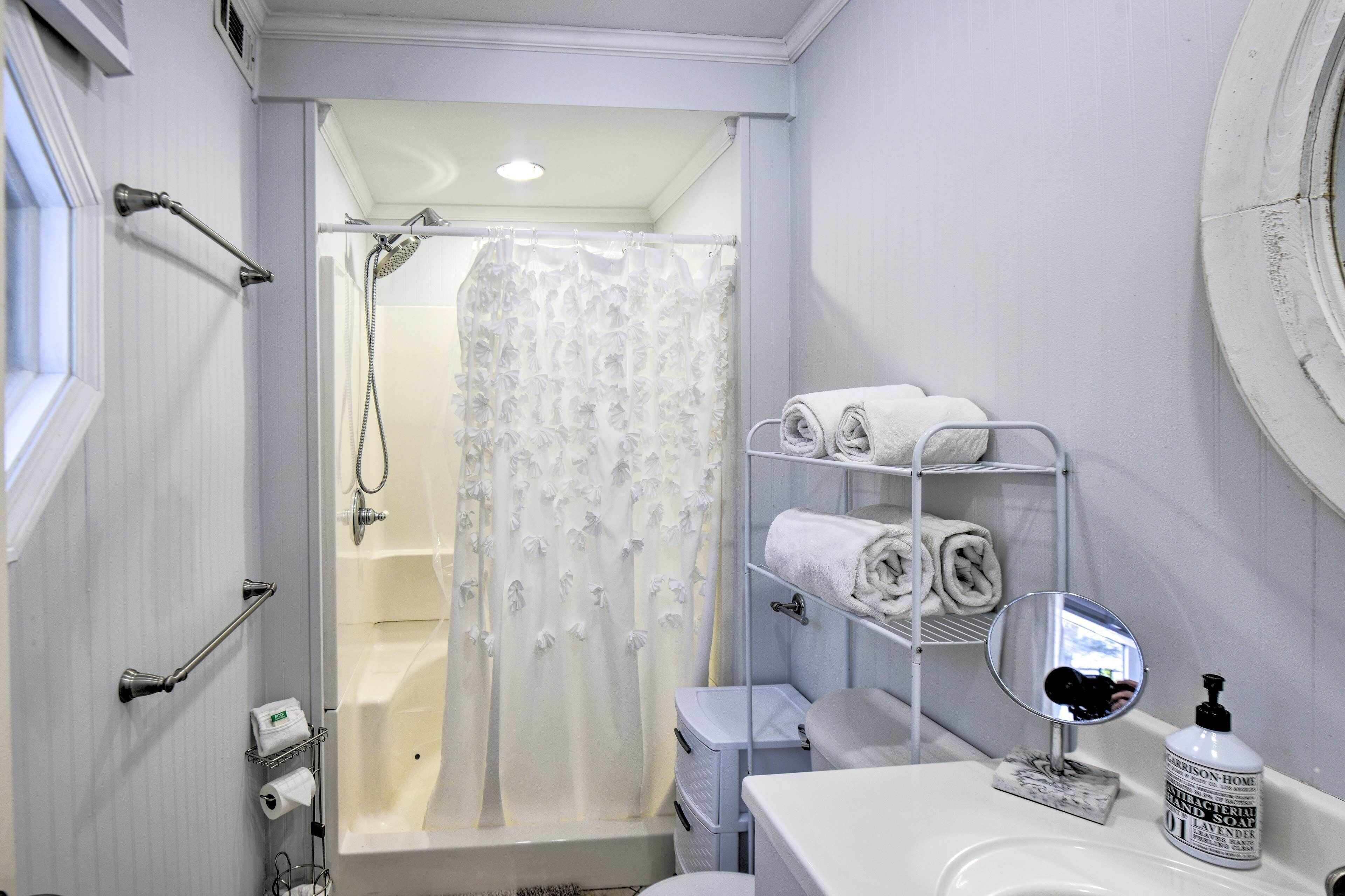 Un baño con ducha, lavamanos, espejo y repisa con toallas.
