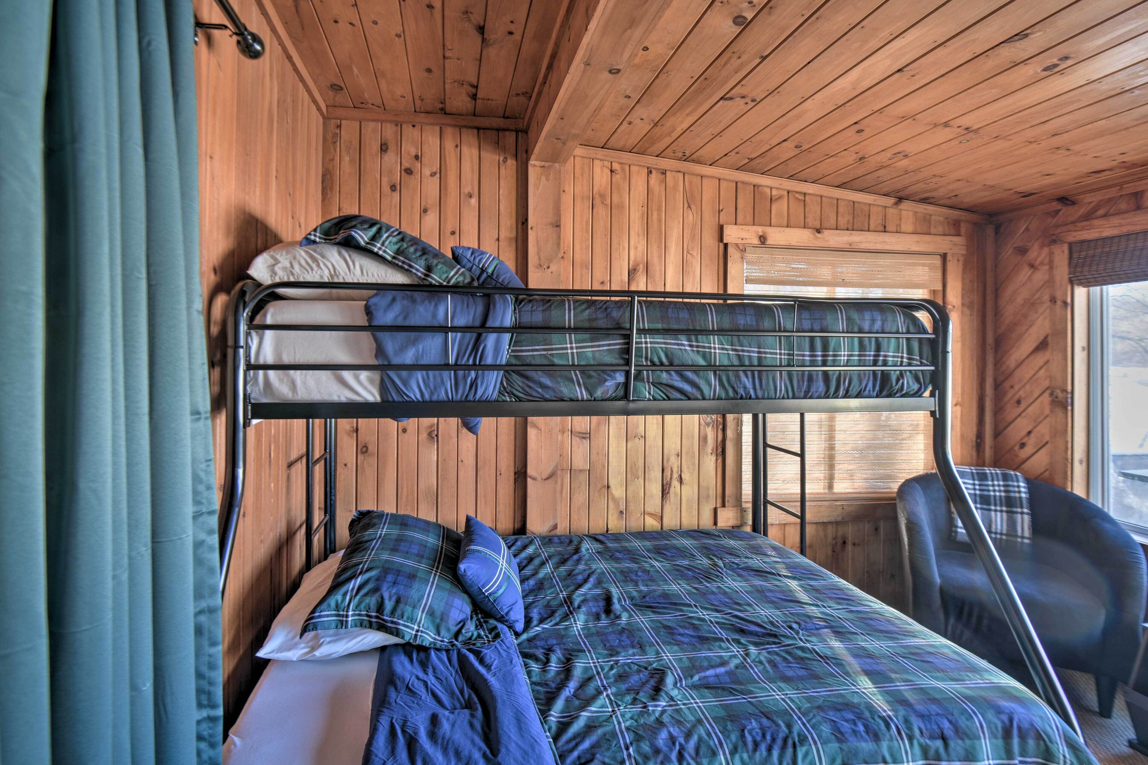 Un lit superposé avec une couette à carreaux et des oreillers, une chaise et des murs en bois.