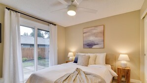 A bedroom with a large bed, two bedside lamps, a ceiling fan, and a view through a sliding glass door. - Lovely Vancouver Retreat w/ Home Gym! (Vancouver)