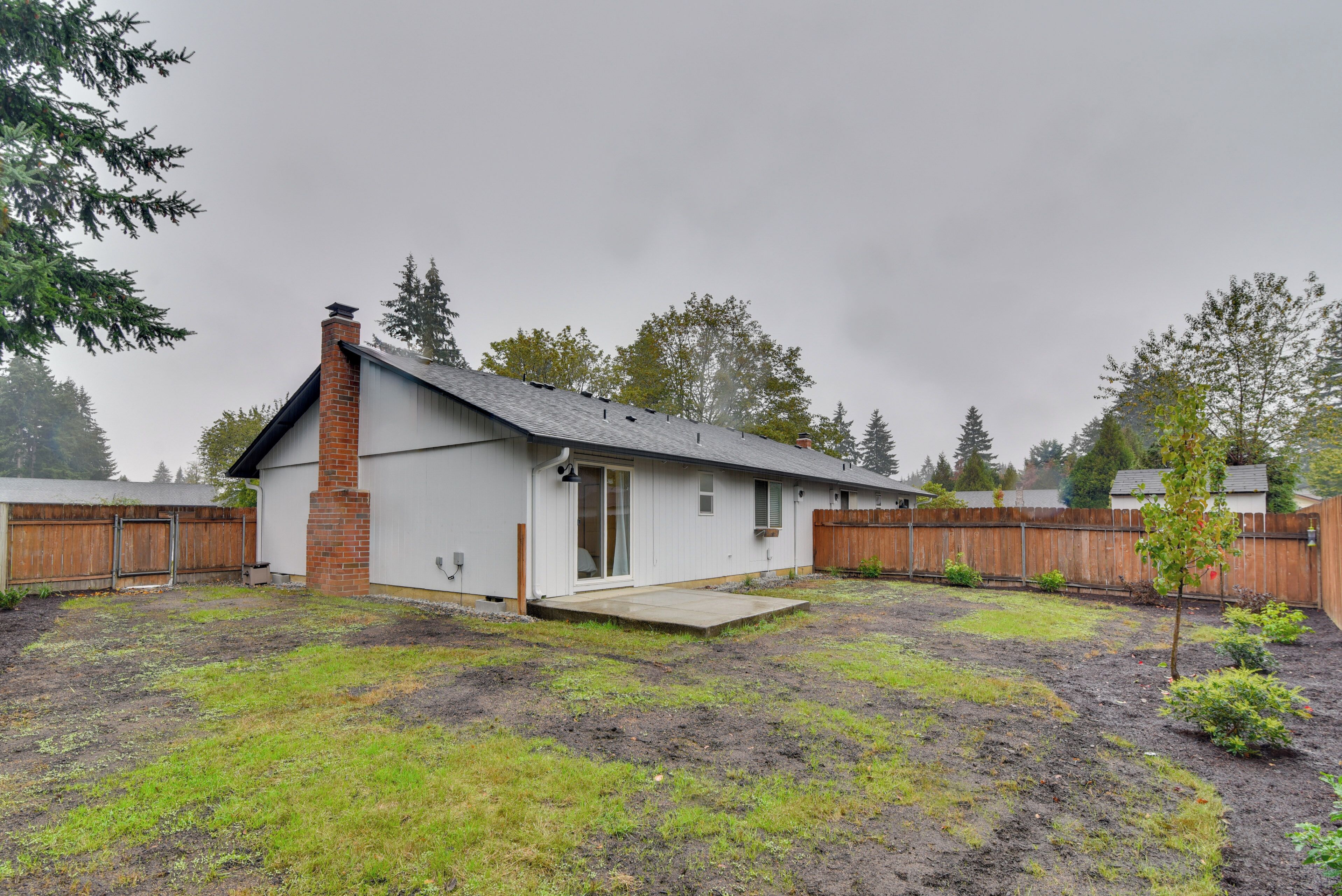 A single-story house with a brick chimney, a small porch, and a fenced backyard.