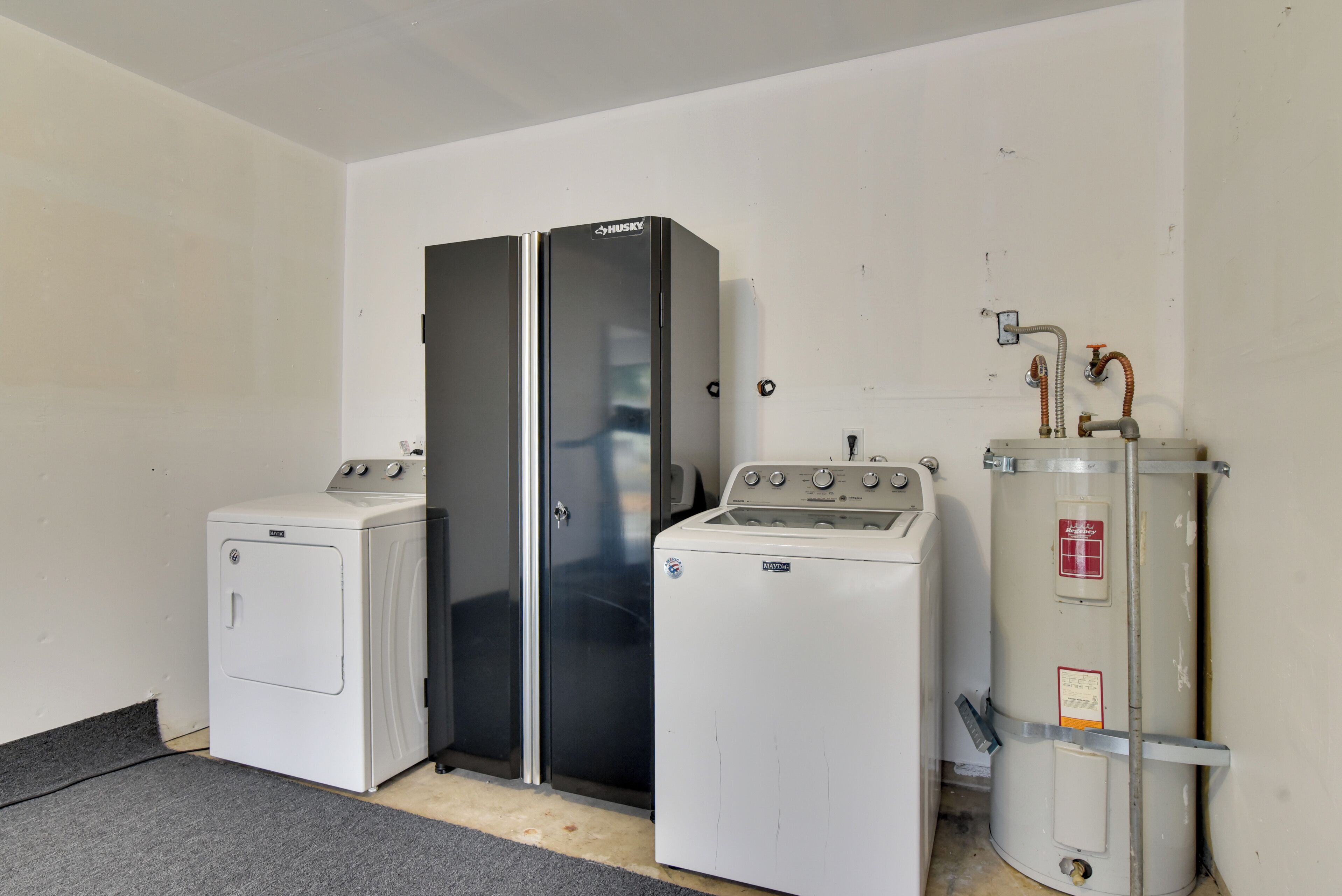 A laundry room with two washers and a dryer, a water heater, and a metal cabinet.