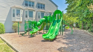 Ein Spielplatz mit grünen Rutschen und Klettergerüsten vor einem zweistöckigen Haus.