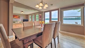 A dining area with a wooden table and chairs, a chandelier, and large windows with a view of a lake. - 13 Mi to Dtwn: Lakefront Cottage w/ Dock (Traverse City)