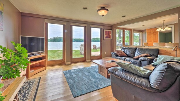 A spacious living room with a large window, a flat-screen TV, a leather sofa, and a wooden coffee table. - 13 Mi to Dtwn: Lakefront Cottage w/ Dock (Traverse City)