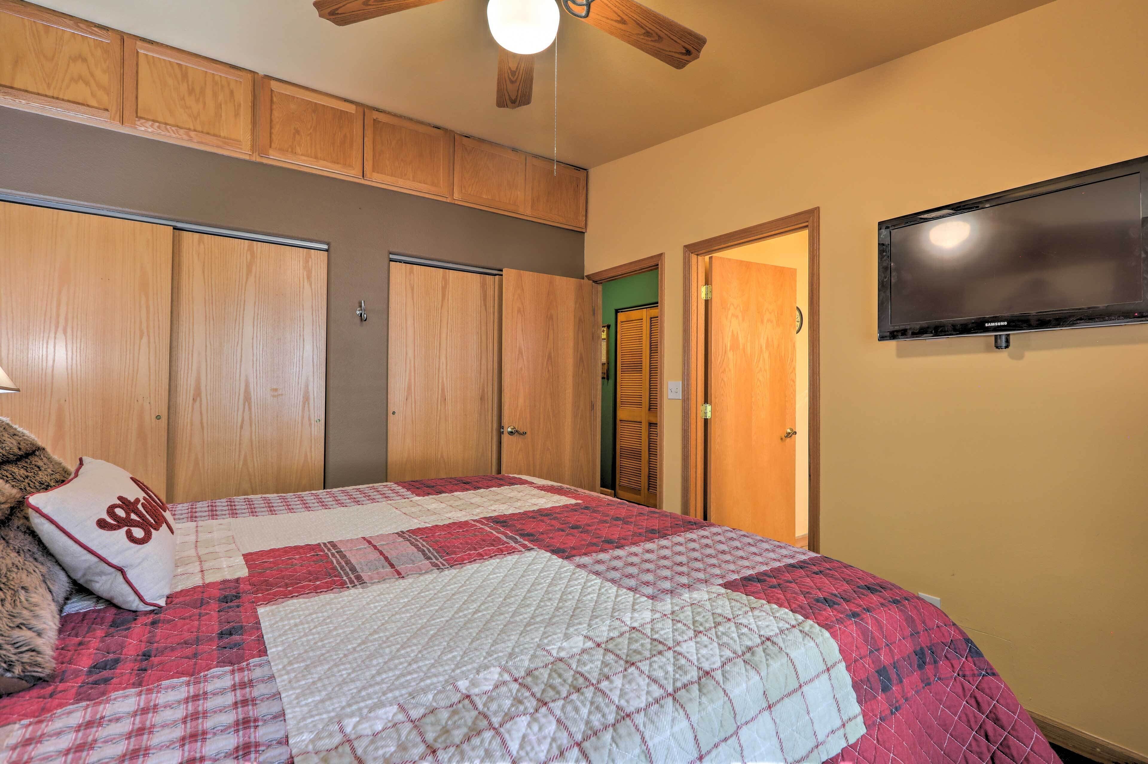 Een slaapkamer met een bed, een houten garderobe, een televisietoestel en een plafondventilator.