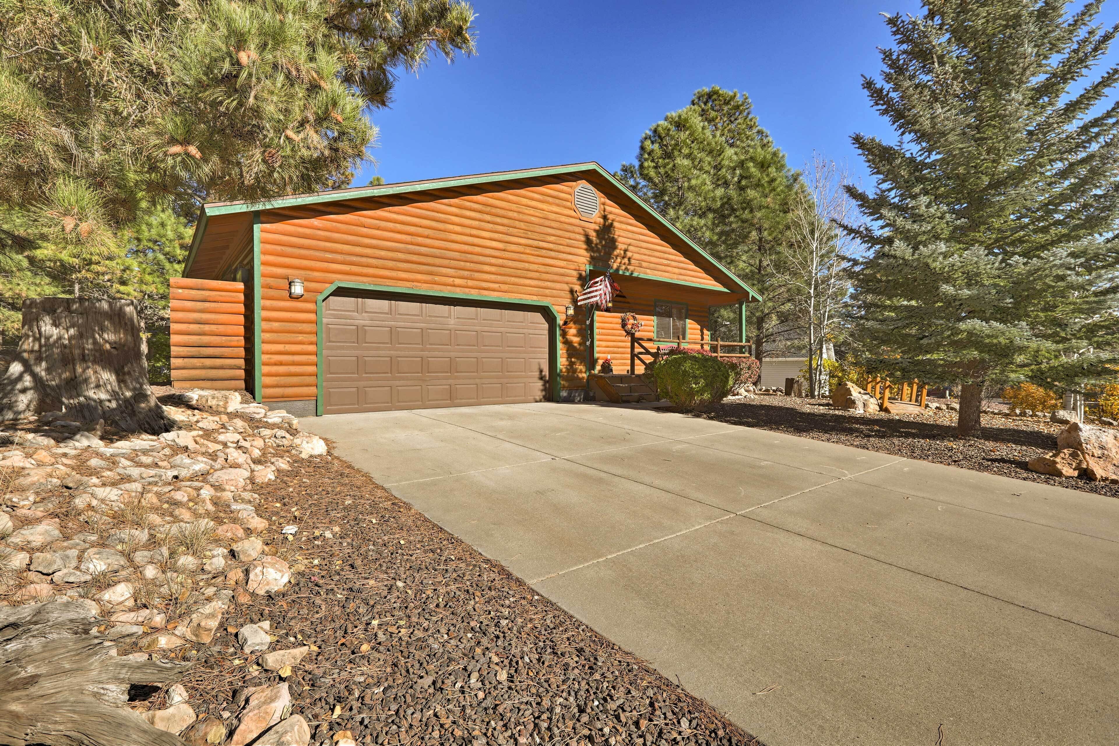 A log cabin with a garage, surrounded by trees and a gravel driveway.