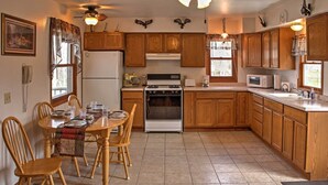 A kitchen with wooden cabinets, a stove, a refrigerator, and a dining table with chairs. - Cozy Balsam Lake Home: Deck, Private Dock + Kayaks (Balsam Lake)