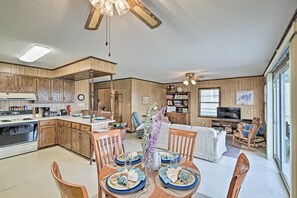 A spacious kitchen with wooden cabinets, a dining area with a table set for four, and a living area with a sofa and TV. - Pet-friendly Second Row House Steps to Beach! (Supply)