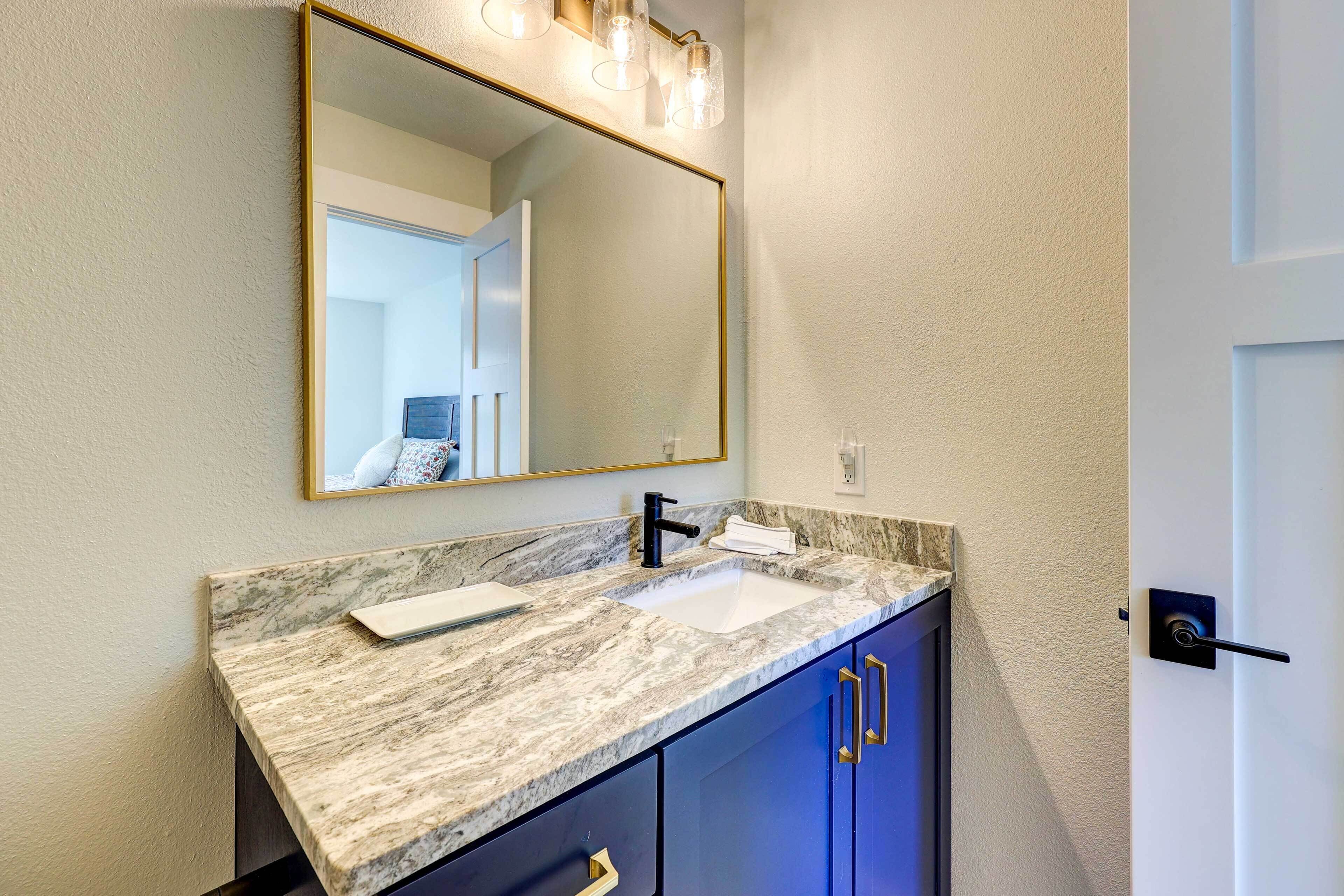 Un baño con encimera de mármol, un lavabo, un espejo con iluminación y armarios azules.