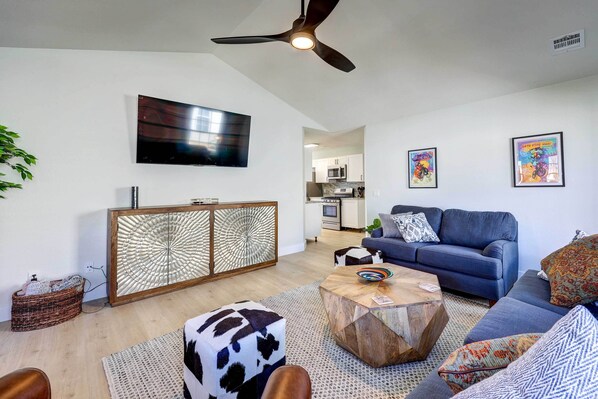 A modern living room with a blue sofa, a wooden coffee table, and a ceiling fan. - Chic Bentonville Home w/ Patio & Fire Pit! (Bentonville)