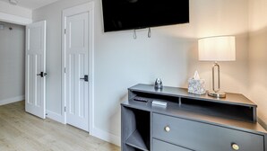 A hotel room with a flat-screen TV mounted on the wall, a desk with a lamp, and a door with a handle.