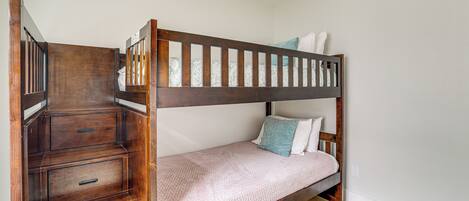 A bunk bed with a wooden frame, a lower drawer unit, and a mattress with pillows.