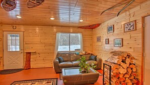 A cozy log cabin interior with a leather sofa, a coffee table with a plant, and a stack of firewood. - 400-acre Outdoor Enthusiast's Lodge in Mancelona! (Mancelona)
