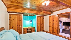Une chambre avec un grand lit, un plafond en bois, un bureau avec une chaise et une vue sur une cheminée en briques.
