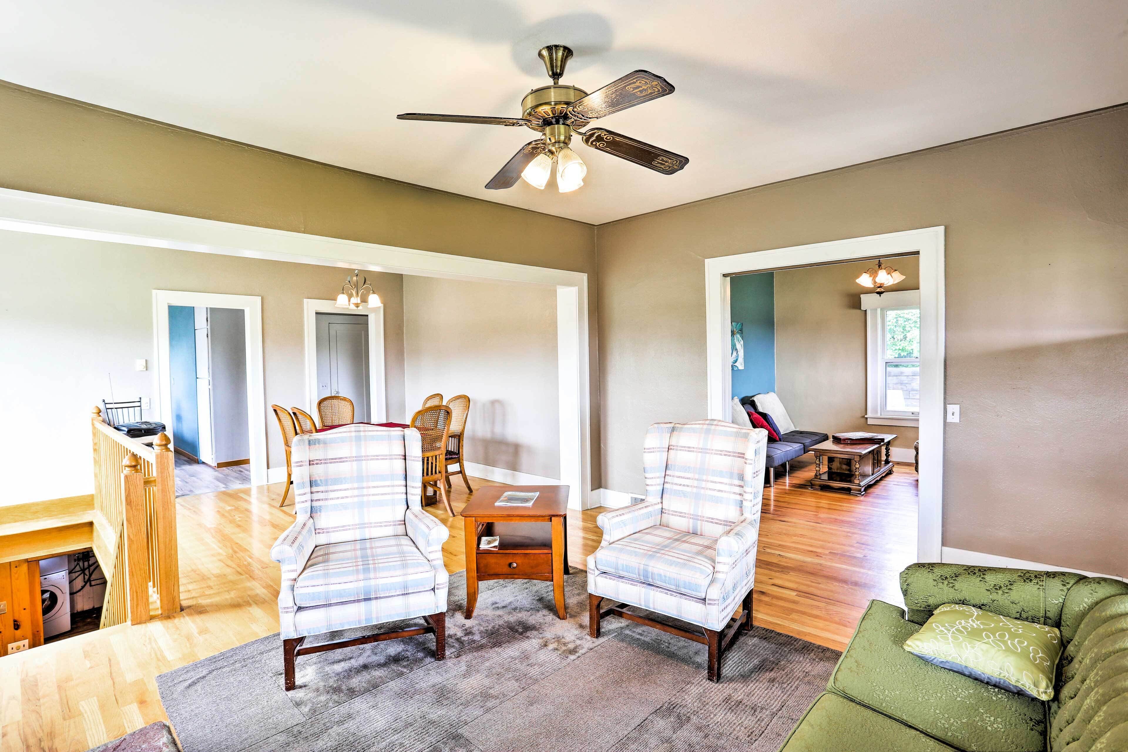 A spacious living room with a ceiling fan, a dining area with a table and chairs, and a green sofa.