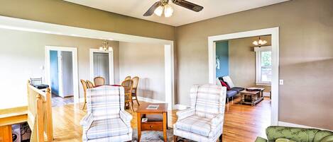 A spacious living room with a ceiling fan, a dining area with a table and chairs, and a green sofa.