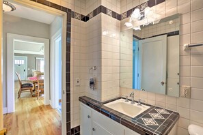 Une salle de bain avec un grand miroir, un lavabo et des toilettes. Une porte donne sur un coin repas équipé de chaises et d’une table.