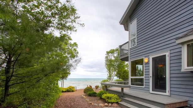 A house with a deck, a view of the ocean, and a gravel pathway leading to the entrance. - Lavish Charlevoix Home on Lake Michigan, Fire Pit (Charlevoix)
