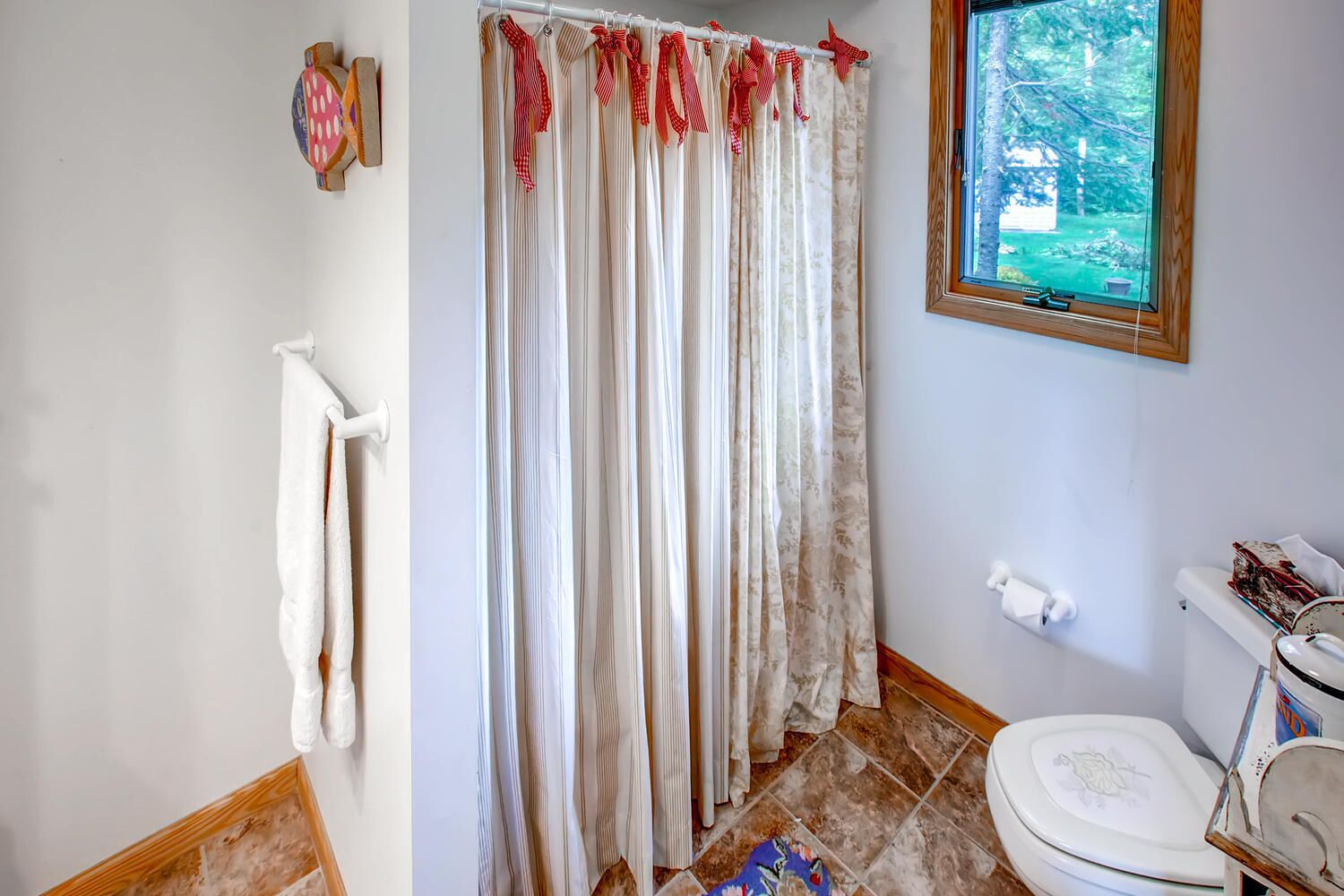 A bathroom with a shower curtain, a toilet, and a window with a view of trees.