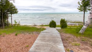 A wooden pathway leading to a beach with a view of the ocean. - Lavish Charlevoix Home on Lake Michigan, Fire Pit (Charlevoix)