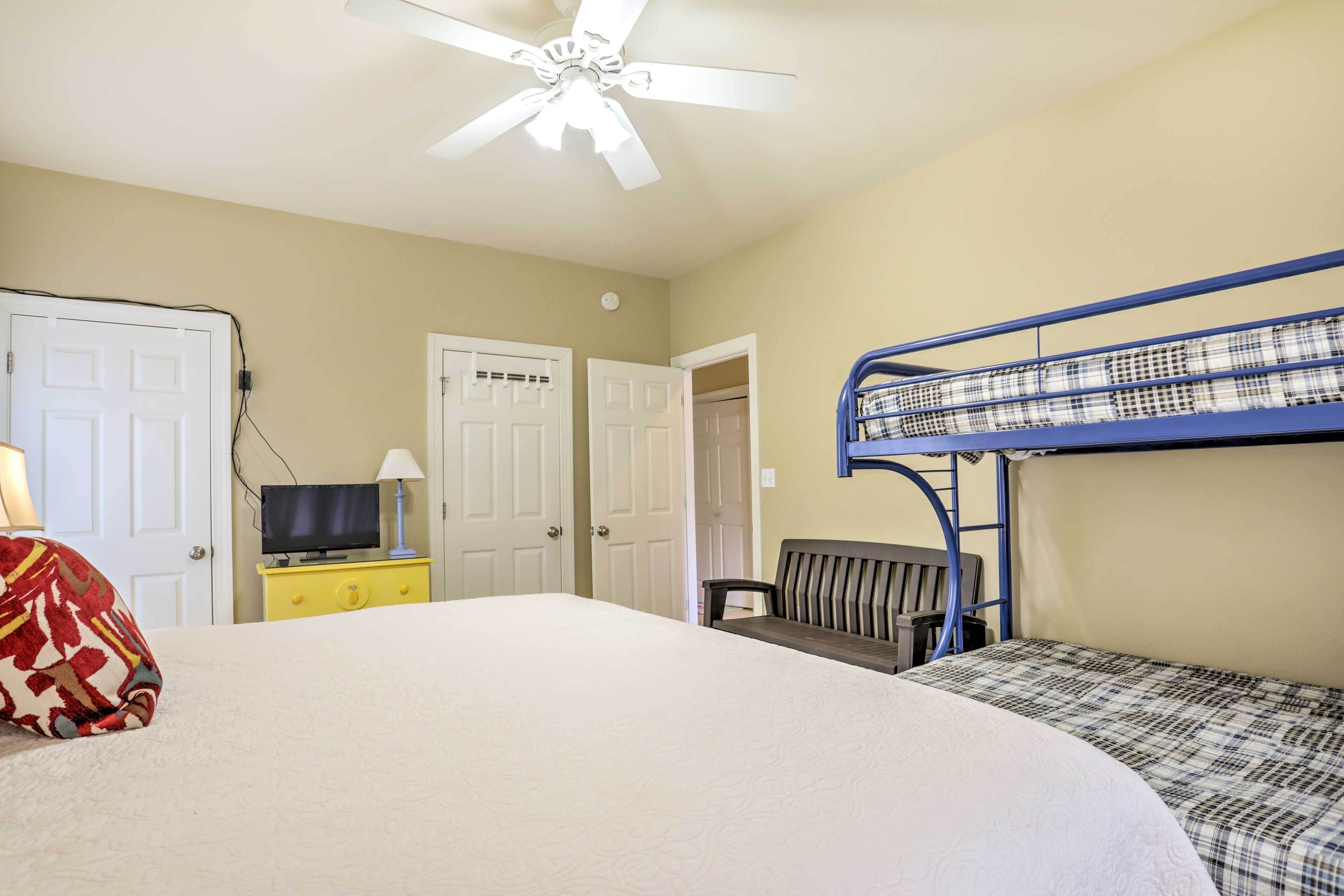 A room with bunk beds, a television on a yellow dresser, and a ceiling fan.