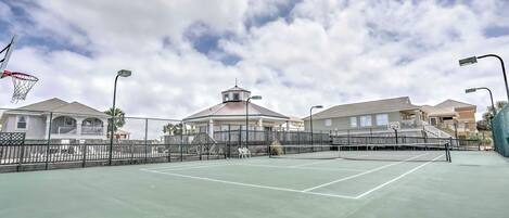 An outdoor tennis court with a net, surrounded by a fence, and adjacent to residential buildings.