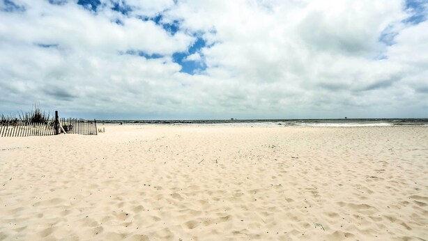 Ein sandiger Strand mit einer Holzzaun und einem bewölkten Himmel.
