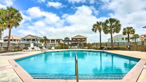 Ein Swimmingpool mit Liegestühlen und Palmen, umgeben von einem Holzzaun und Gebäuden im Hintergrund.