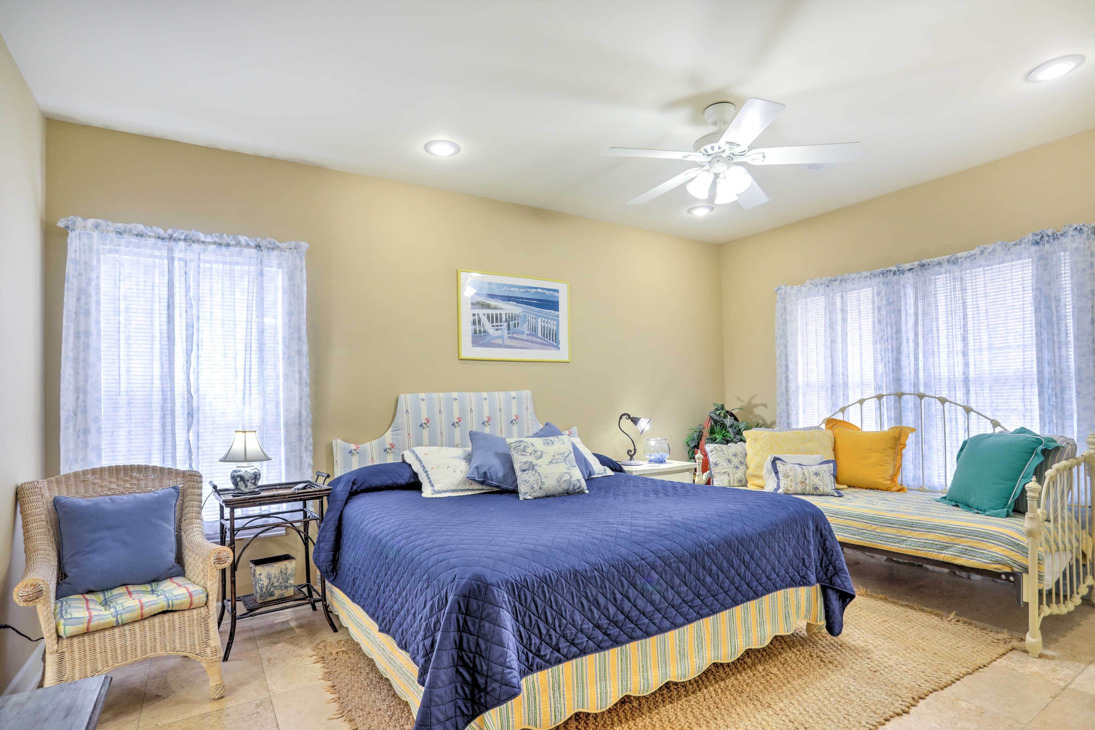 A bedroom with two beds, a wicker chair, a bedside table, and a ceiling fan.