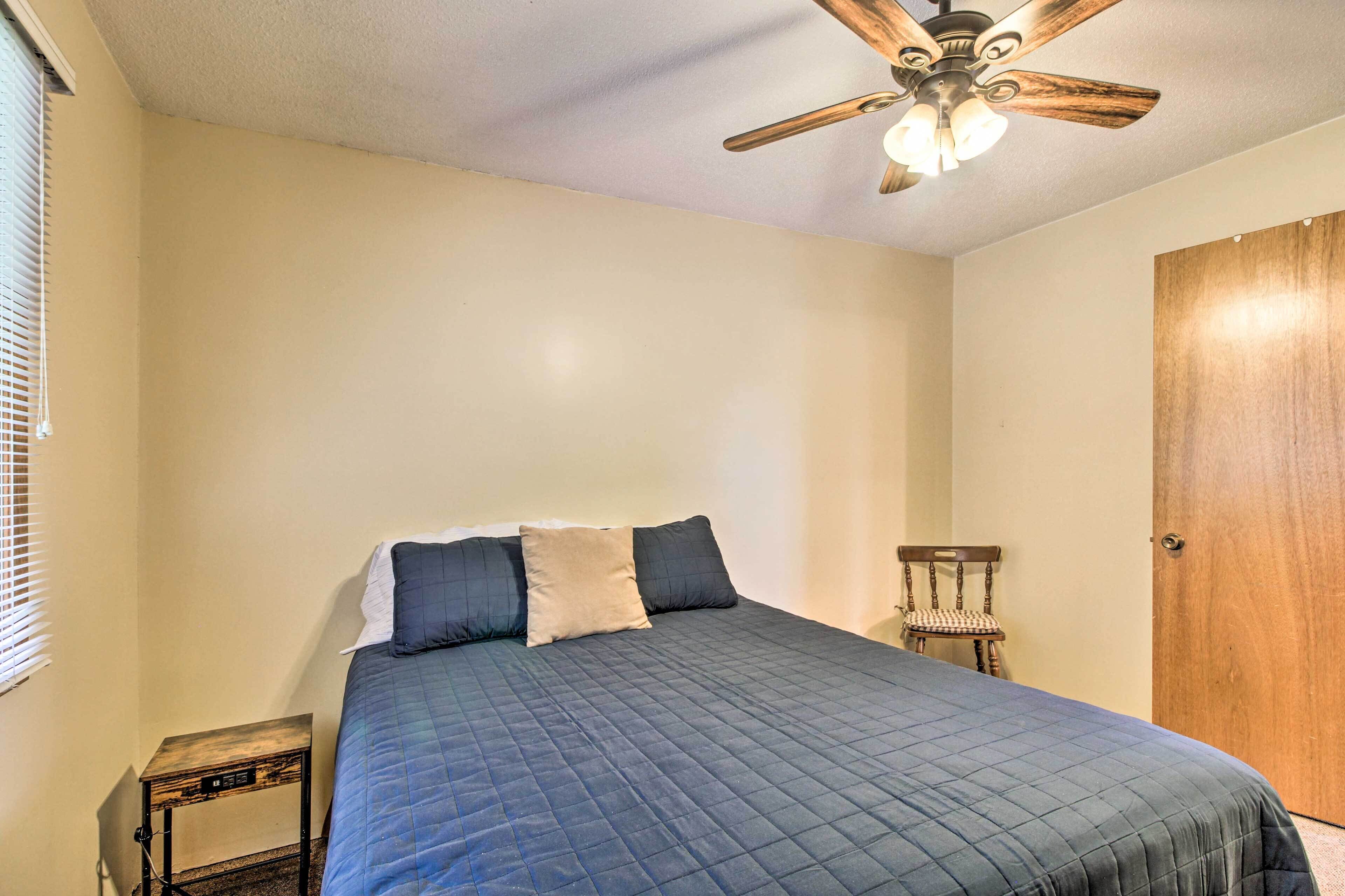 A bedroom with a bed, a ceiling fan, a wooden door, and a small table.