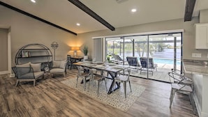 A spacious living area with a dining table, chairs, and a sofa. There is a large window with a view of a pool and outdoor seating. - Canal-front Cape Coral Home: Pool & Patio (Cape Coral)