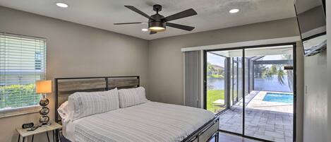 Un dormitorio con cama, ventilador de techo, mesita de noche con lámpara y vista a una piscina a través de una puerta corrediza de vidrio.