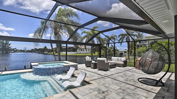 A pool area with a hot tub, lounge chairs, and a seating area with a woven chair. - Canal-front Cape Coral Home: Pool & Patio (Cape Coral)
