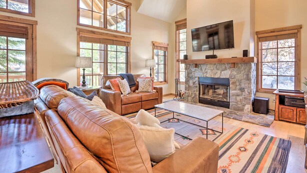A spacious living room with a stone fireplace, leather sofas, and a television mounted on the wall.